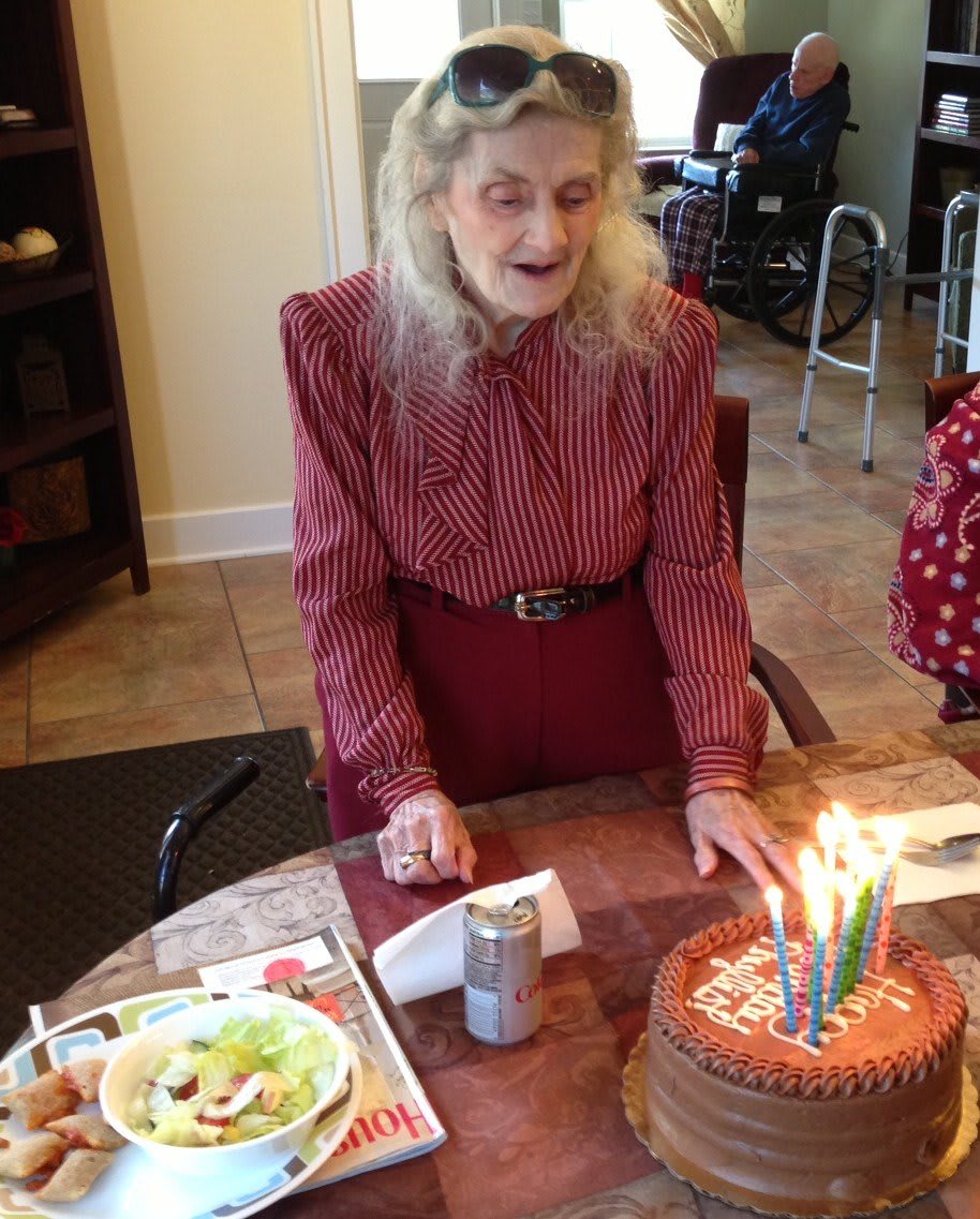An elderly woman celebrates her birthday with a cake and lit candles.