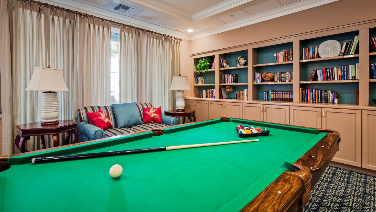 A cozy living room with a pool table and bookshelves, featuring comfortable seating and decorative elements.