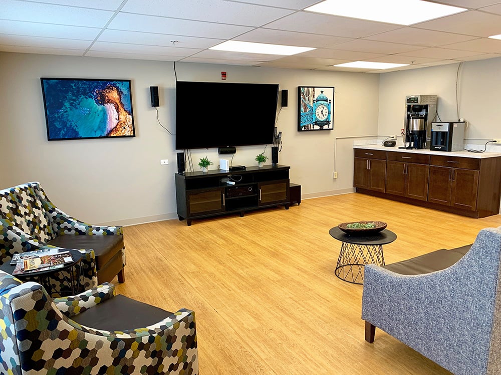 A modern lounge area with a television, comfortable seating, artwork on the walls, and a coffee station.