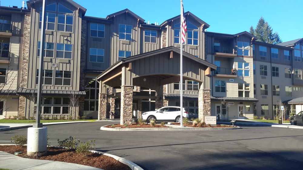 A modern building entrance with a car parked under the portico and an American flag flying nearby.
