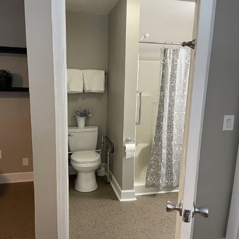 A modern bathroom with a toilet and shower viewed through an open door.