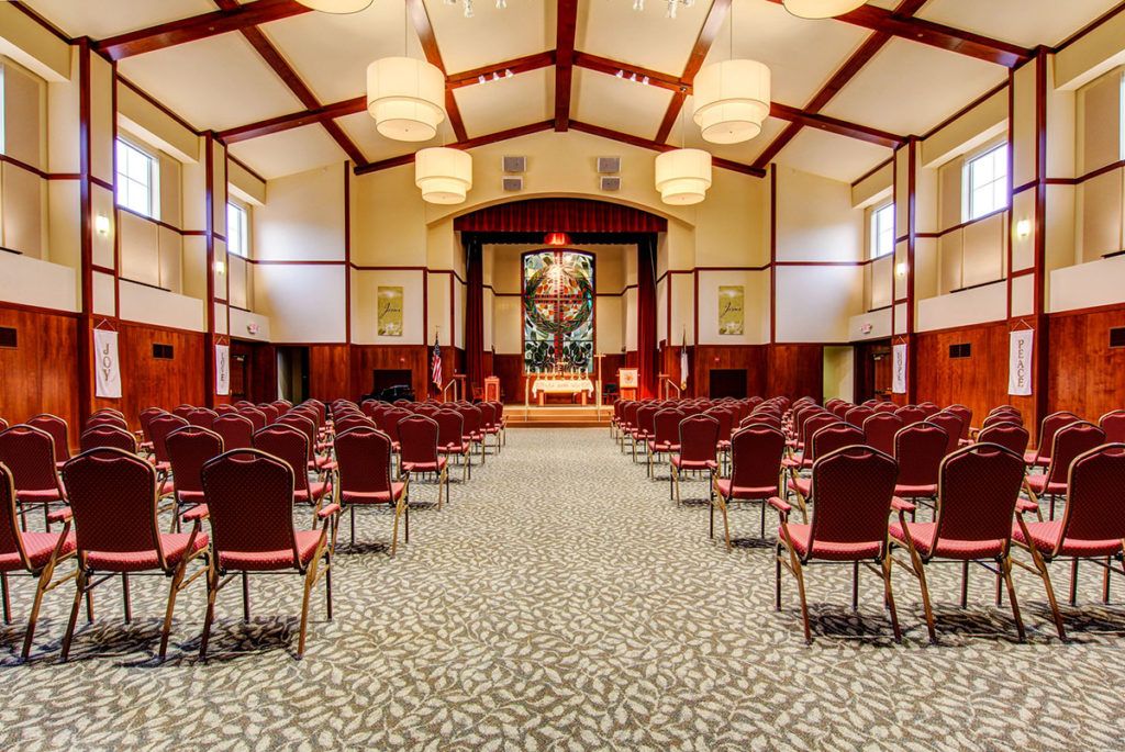 An interior view of a chapel with rows of chairs and stained glass windows.
