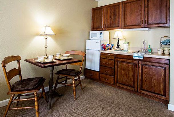A cozy kitchen and dining area with wooden cabinets, a small table with chairs, and soft lighting from table lamps.