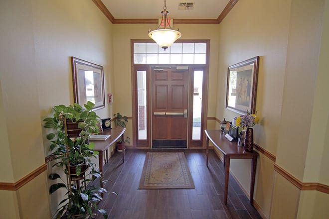 An inviting hallway with a wooden door, decorated with plants and mirrors on side tables.