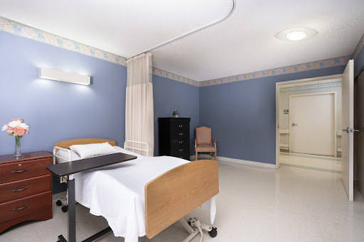 A clean and well-lit hospital patient room featuring a bed, curtains, and a dresser.