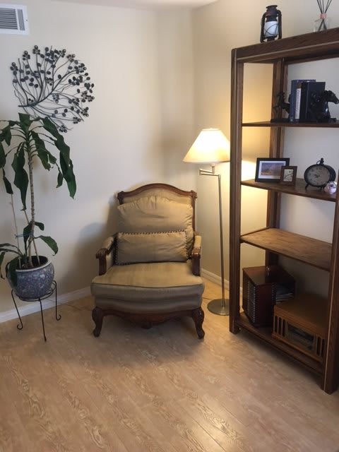 A cozy corner with an armchair, floor lamp, and bookshelf beside a potted plant.