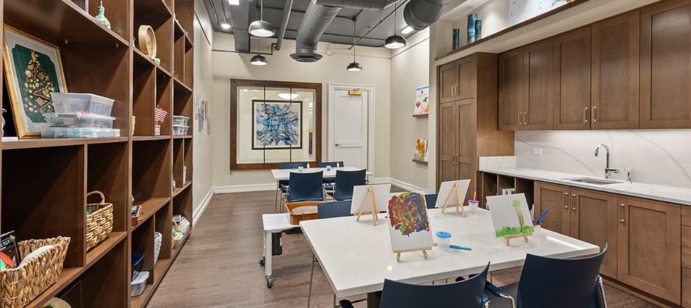 A modern art studio with tables and chairs, featuring paintings and art supplies.