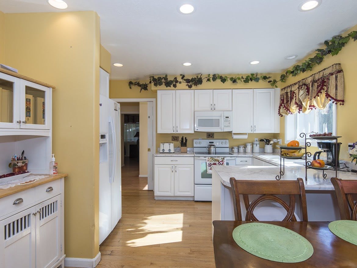 A bright kitchen with yellow walls, white cabinets, and decorative plants above the cabinets.