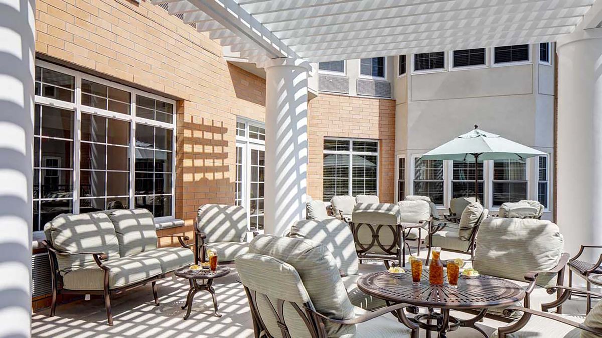A sunny patio with comfortable seating and tables under a pergola.