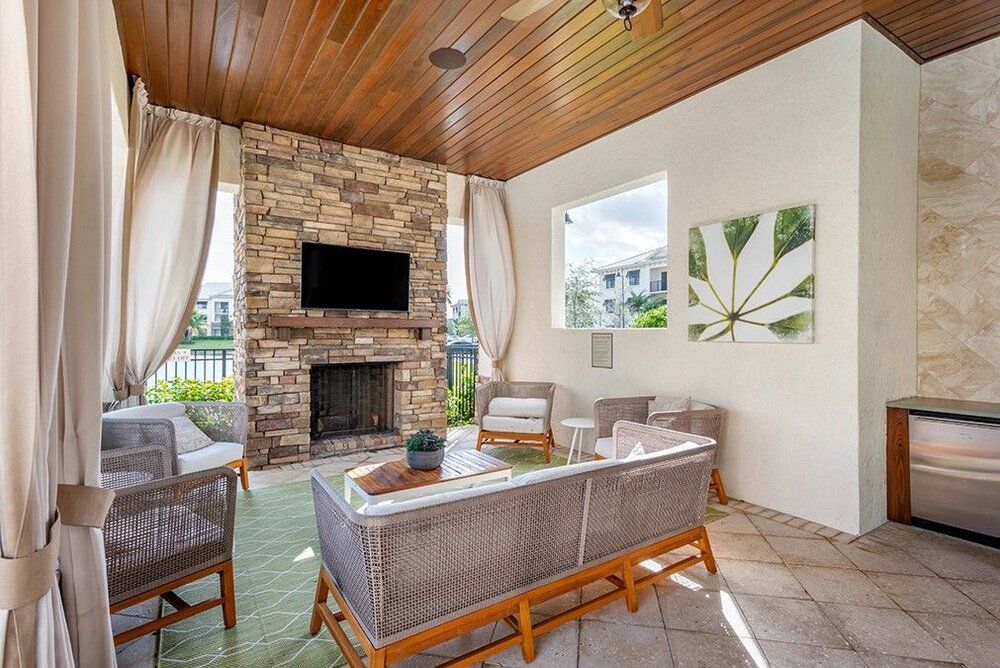 A stylish outdoor living space featuring a cozy seating area, stone fireplace, and television, all under a wood-paneled ceiling.