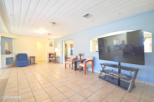 A spacious living room featuring blue walls and tiled flooring, equipped with modern furniture and a large television.