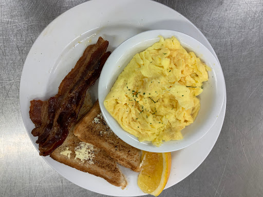 A hearty breakfast plate featuring scrambled eggs, crispy bacon, and toast with an orange slice.