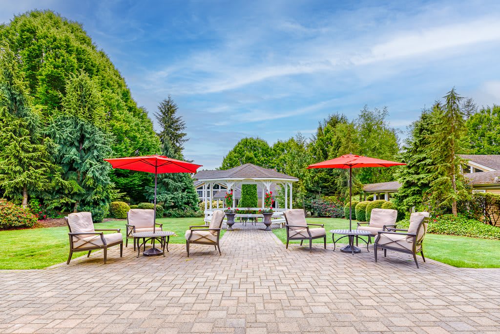 A beautiful garden patio with chairs and umbrellas overlooking a gazebo.