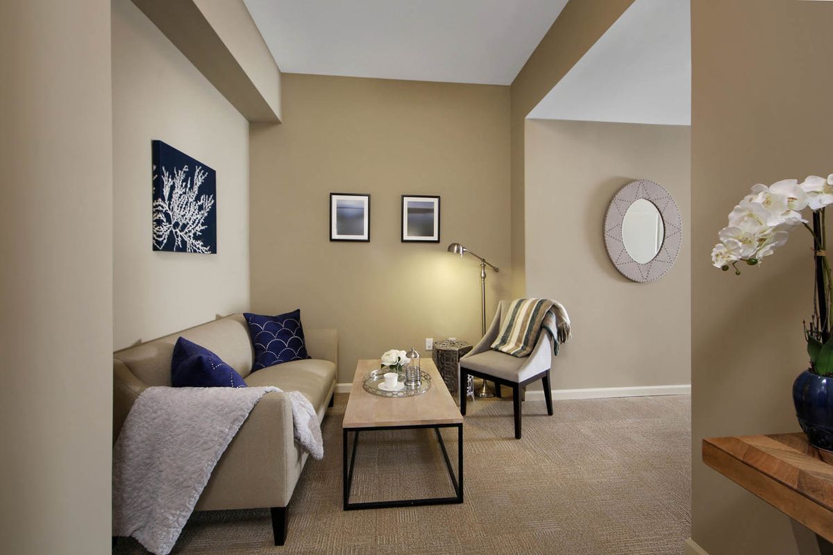 A cozy living room with a beige color scheme, featuring a sofa, armchair, coffee table, and decorated with wall art and a mirror.