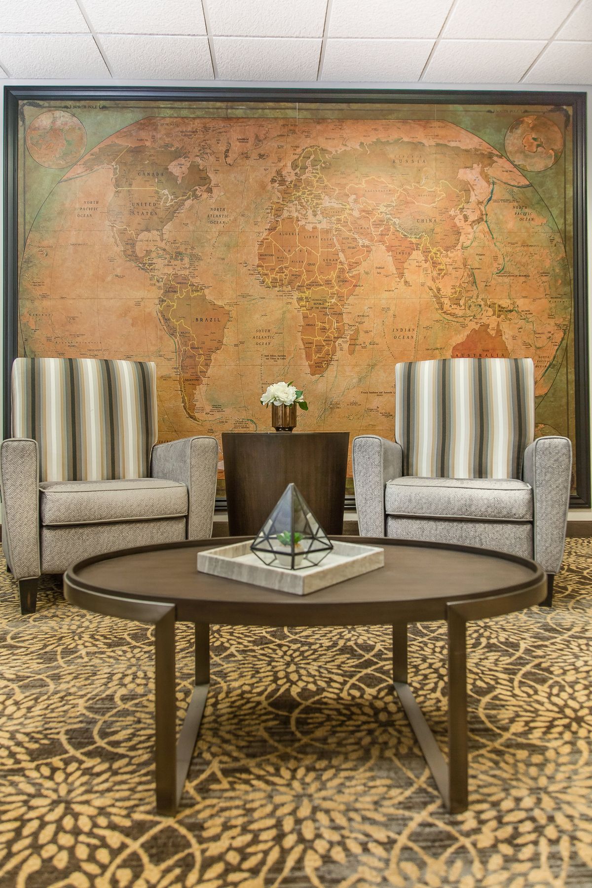 A stylish living room with striped chairs, a round coffee table, and a large world map on the wall.