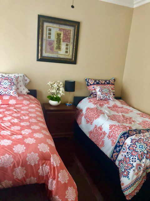 A cozy bedroom featuring two twin beds with floral patterned bedding, separated by a nightstand and adorned with wall art.