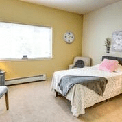A cozy bedroom with a bed, armchair, and natural light from the window.
