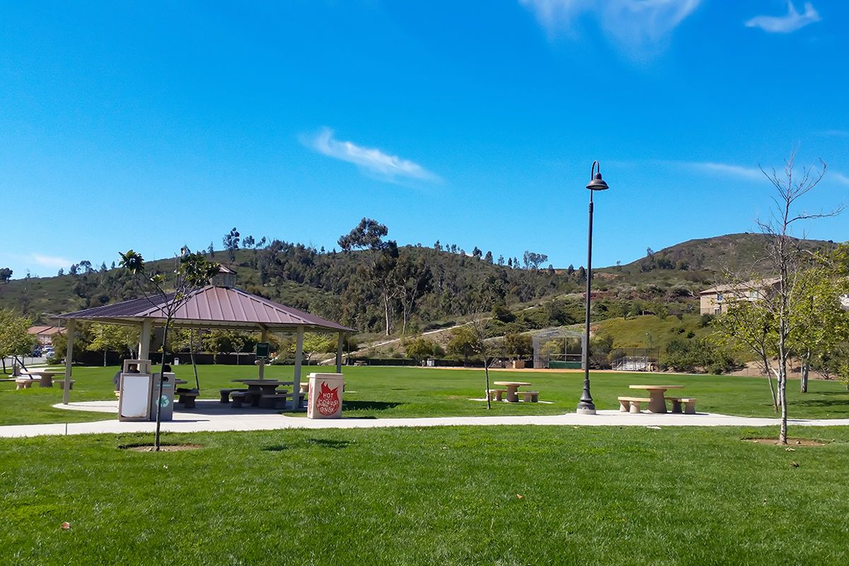 A scenic park with a pavilion, picnic tables, and lush green fields under a clear blue sky.