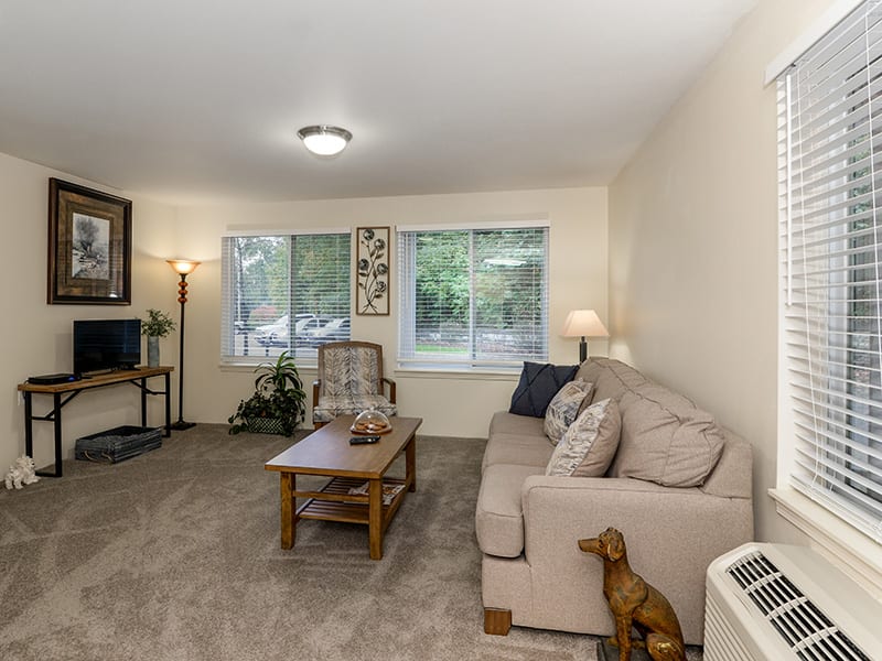 A cozy living room with a sofa, coffee table, and large windows letting in natural light.
