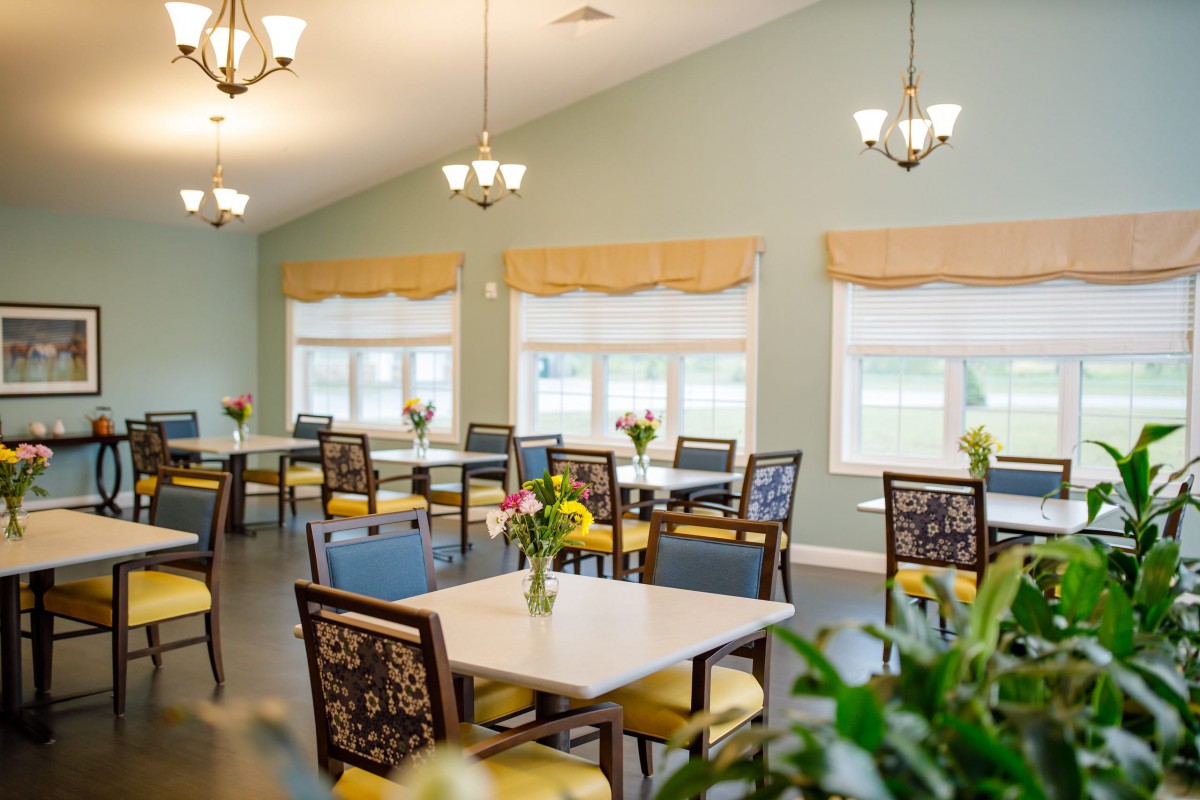 A bright and inviting dining room with neatly arranged tables and chairs, illuminated by chandeliers.