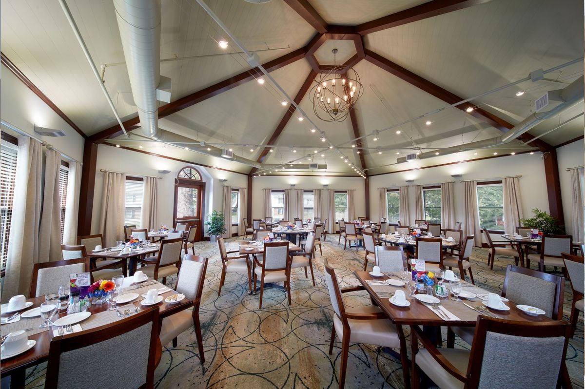 A spacious and elegantly designed dining area with neatly arranged tables and chairs, illuminated by a central chandelier.