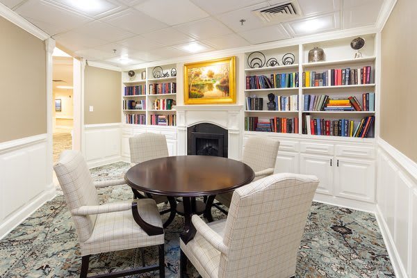 A cozy library room with a round table and chairs surrounded by bookshelves and artwork.