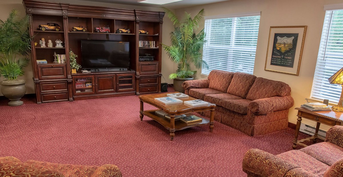 A cozy living room with a large entertainment center, comfortable sofa, and coffee table on a red carpet.