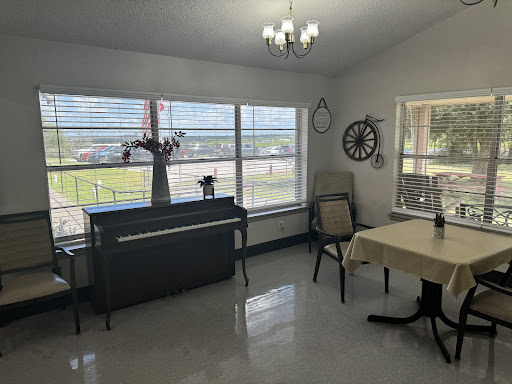 A bright and spacious room featuring a piano, dining table, and large windows.