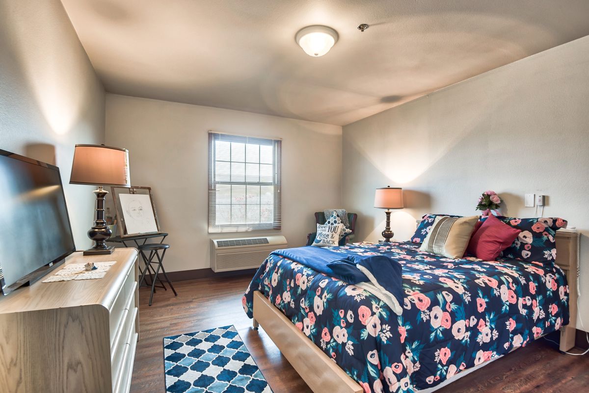 A cozy bedroom interior with floral bedding, two lamps, and a window illuminating the space.