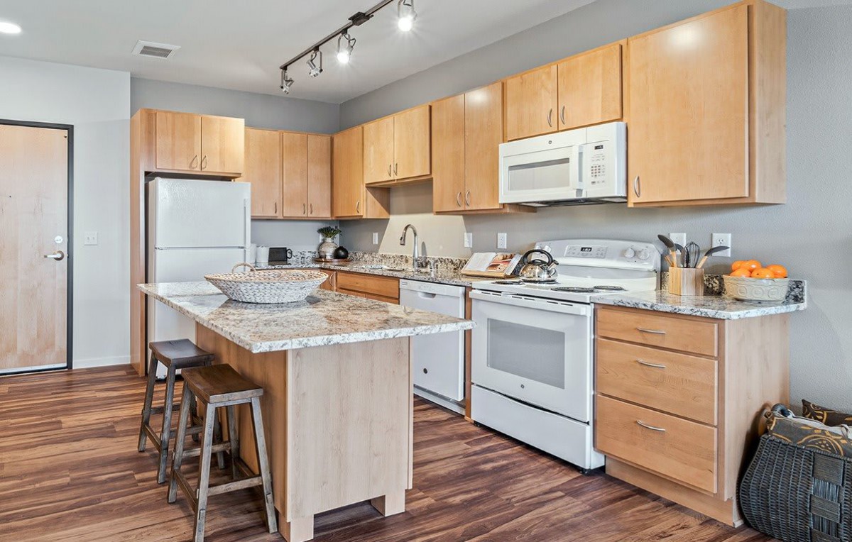 A modern kitchen with wooden cabinets, featuring a central island with stools and various appliances.