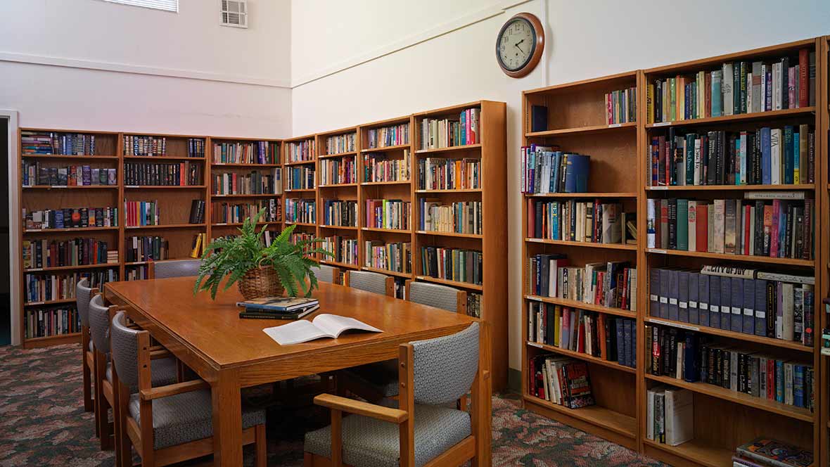 A quiet library room with bookshelves filled with books and a table surrounded by chairs.