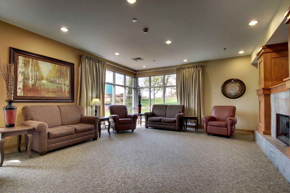 A cozy living room with sofas and armchairs, featuring large windows and warm lighting.