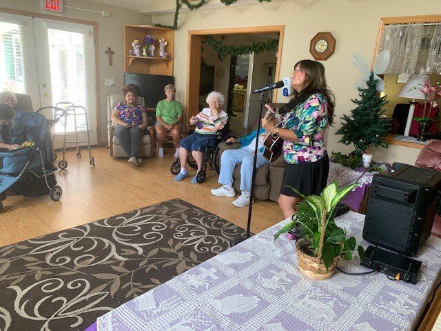 A person is playing guitar for a group of seniors in a nursing home living room.