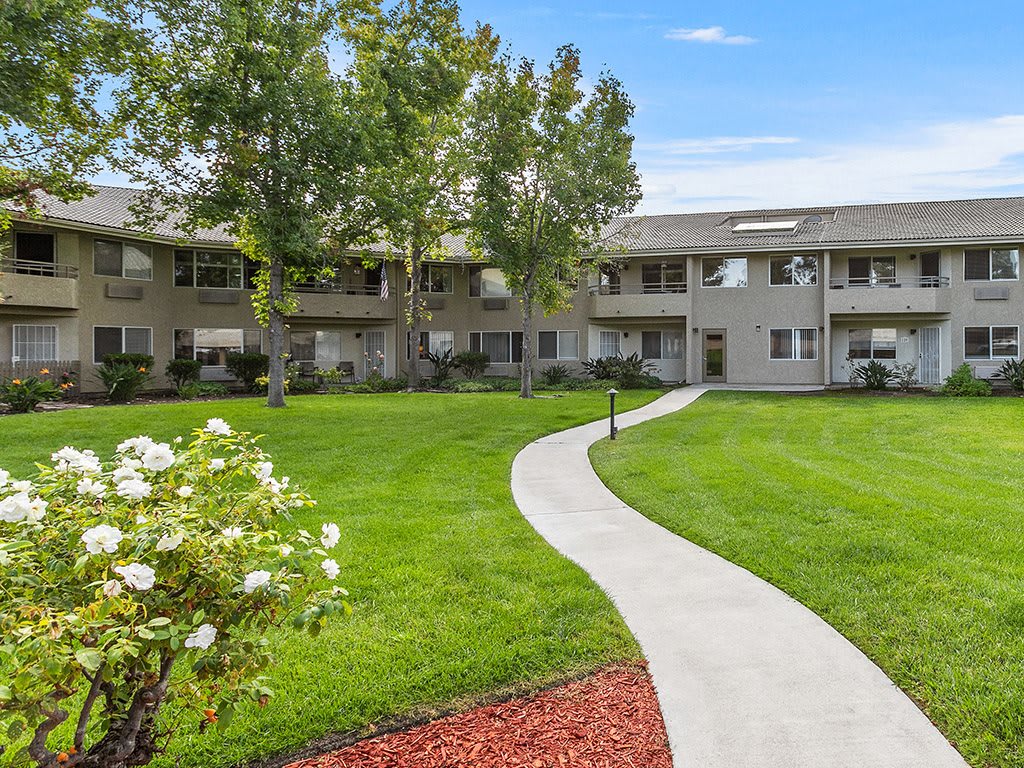 A well-maintained apartment complex with a landscaped lawn and a winding pathway.