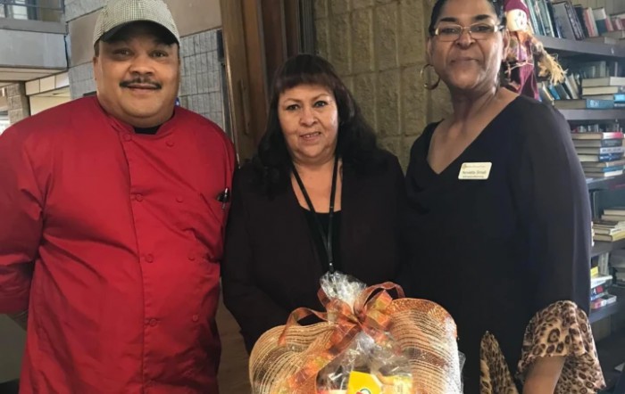 Three individuals posing with a wrapped food gift basket.