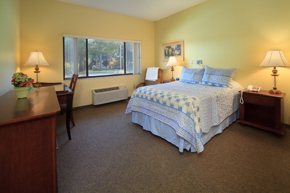 A cozy bedroom with a neatly made bed, a desk, and a large window.