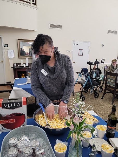 A woman wearing a mask is preparing food at an indoor event, with decorations and a food table set up.