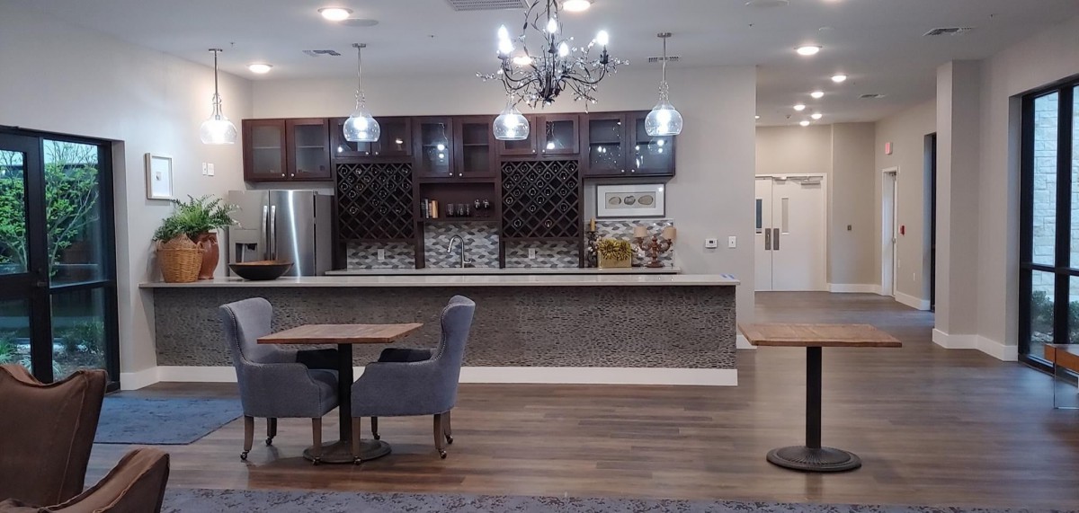 A cozy kitchen and bar area with a chandelier, featuring wooden flooring and comfortable seating.