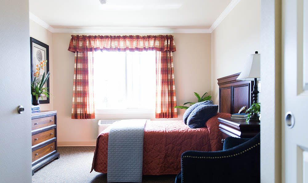A cozy bedroom with a bed near a sunlit window and decorative curtains.
