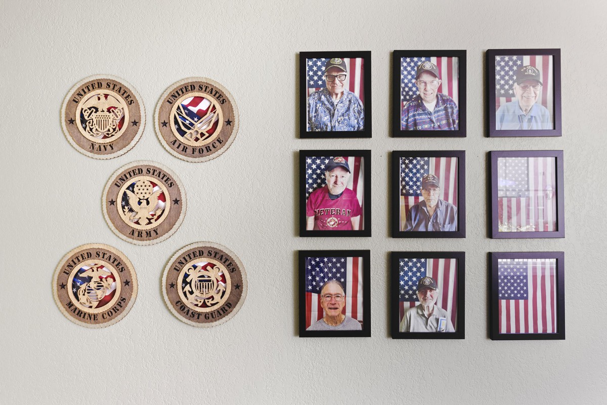 A wall display featuring military insignia and framed portraits of veterans with an American flag backdrop.