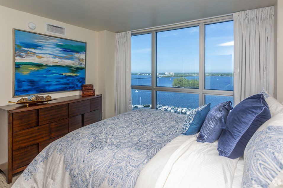 A modern bedroom with a stunning ocean view through large windows, featuring stylish decor and artwork.