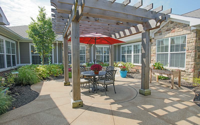 A cozy patio with a pergola, featuring a red umbrella and outdoor seating.