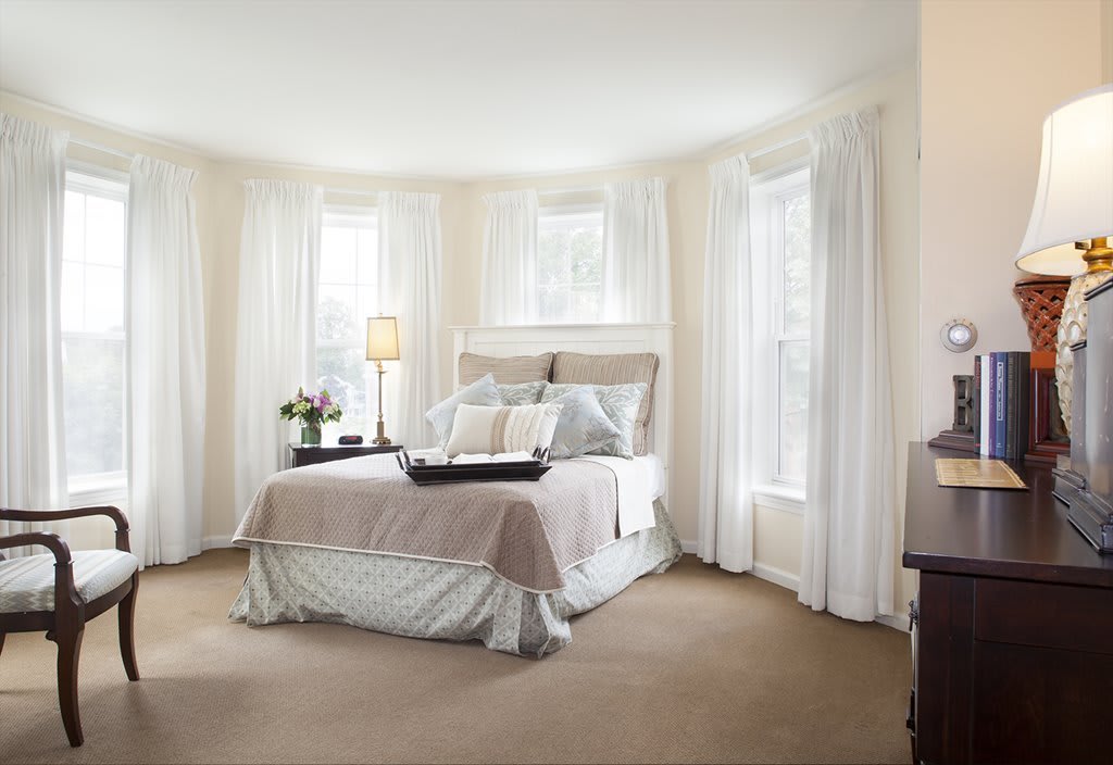 A beautifully designed bedroom with neutral tones and large windows adorned with curtains.