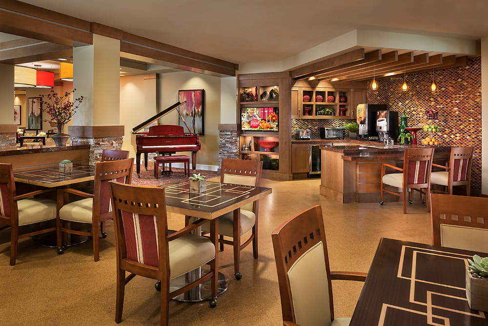 A cozy dining area with a bar and seating, featuring a red piano in the background.