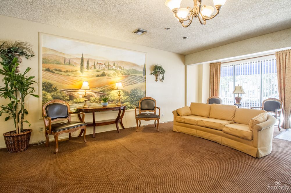 A cozy living room with a mural on the wall, featuring a sofa, chairs, and a chandelier.