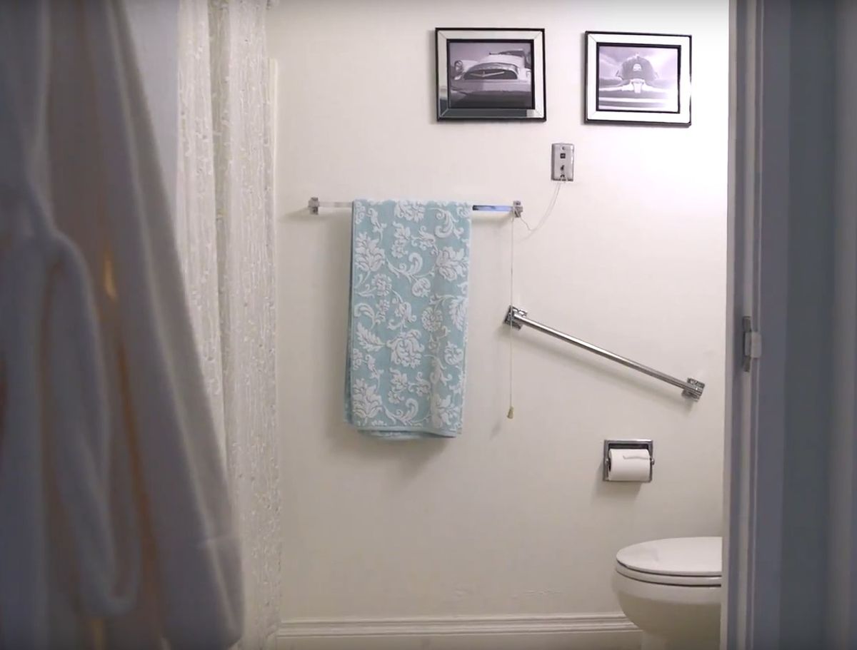 A bathroom with a patterned towel, grab bar, toilet, and framed pictures on the wall.
