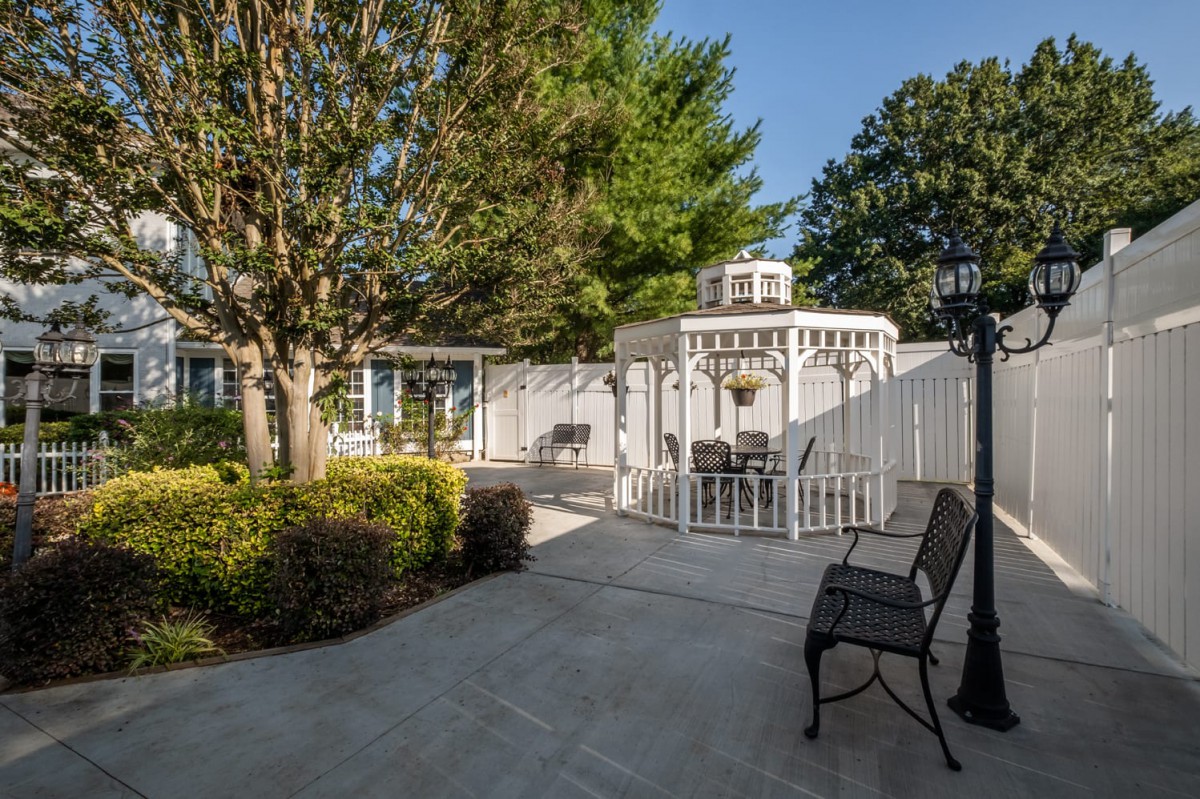 A peaceful garden with a white gazebo and outdoor seating, surrounded by lush greenery.