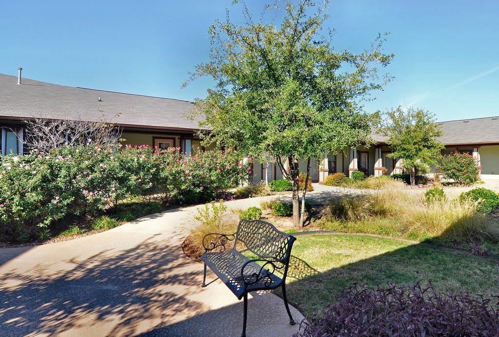 A peaceful courtyard with a bench and landscaped greenery in front of a building.