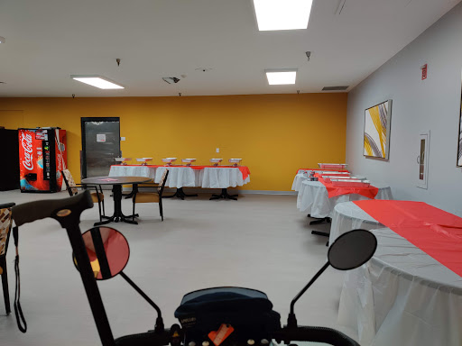 A spacious dining area with tables set with red tablecloths against a vibrant yellow wall.