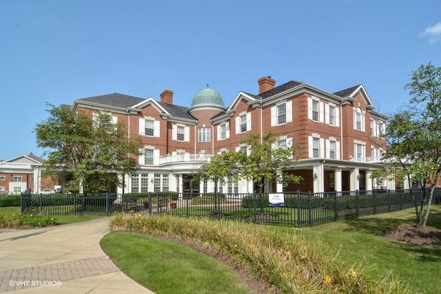 A large, red-brick residential building with a manicured garden and clear blue sky.